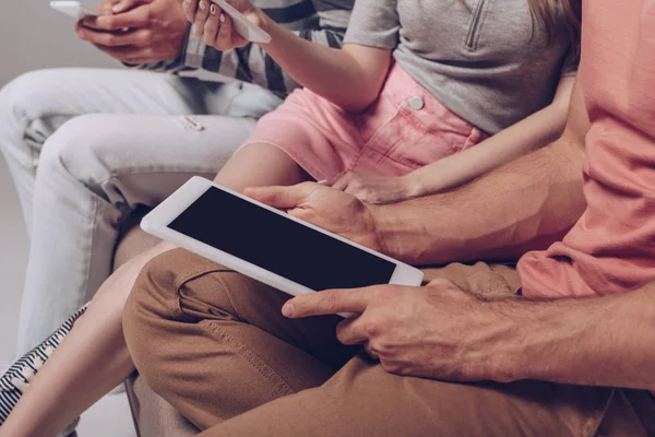 Vista recortada de amigos usando dispositivos digitales con pantalla en blanco mientras están sentados juntos - foto de stock