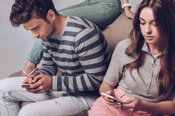 Hermosos amigos usando teléfonos inteligentes mientras están sentados juntos aislados en gris - foto de stock