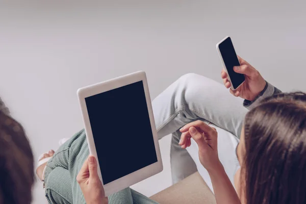 Vue recadrée du couple à l'aide d'un smartphone et d'une tablette numérique avec des écrans vides tout en étant assis ensemble isolé sur gris — Photo de stock