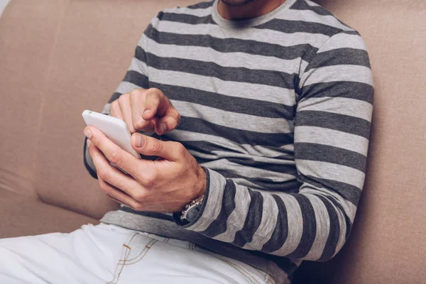 Partial view of man using smartphone and sitting on sofa — Stock Photo