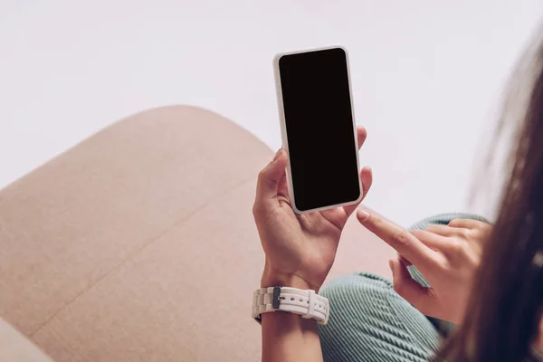 Обрезанный вид девушки с помощью смартфона с пустым экраном, сидя на диване изолированы на сером — стоковое фото