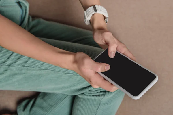 Cropped view of girl using smartphone with blank screen while sitting on sofa — Stock Photo