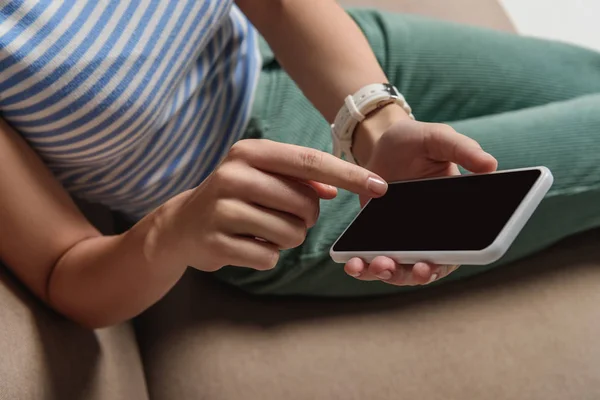 Abgeschnittene Ansicht einer Frau, die Smartphone mit leerem Bildschirm benutzt, während sie auf dem Sofa sitzt — Stockfoto