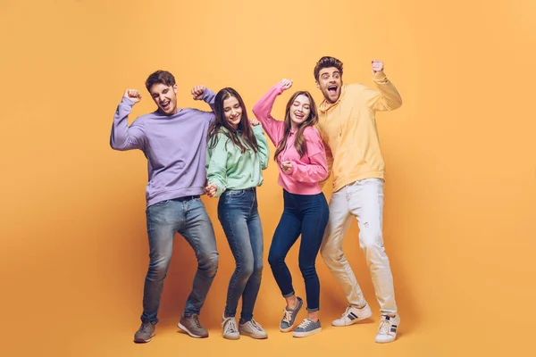 Jovens amigos felizes dançando juntos, no amarelo — Fotografia de Stock