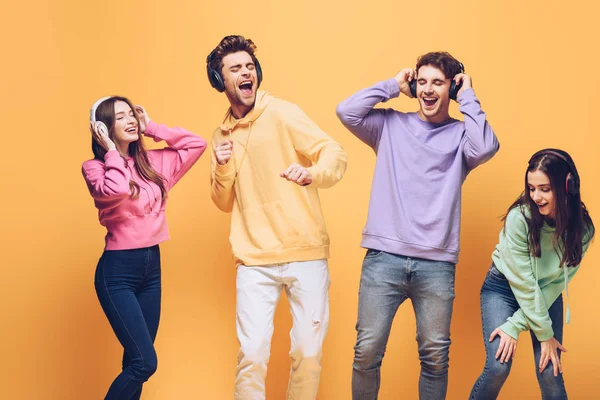 Positive Freunde, die Musik über Kopfhörer hören und zusammen tanzen, isoliert auf gelb — Stockfoto