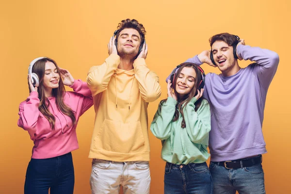 Amigos alegres escuchando música en auriculares y bailando juntos, aislados en amarillo - foto de stock