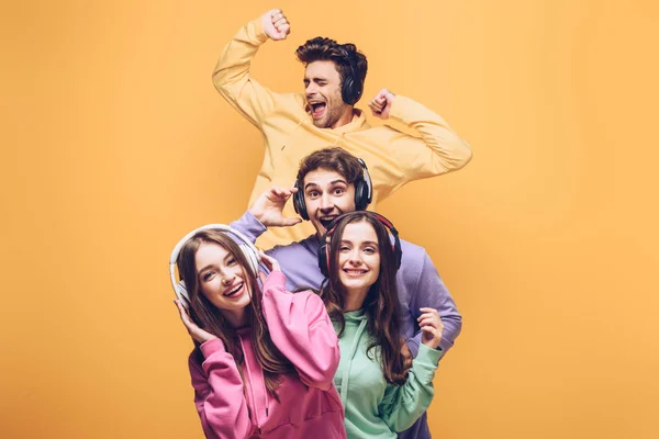 Emotional friends listening music in headphones and dancing together, isolated on yellow — Stock Photo