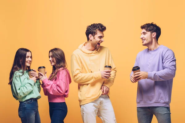 Amigos sorridentes conversando e segurando café para ir, isolado em amarelo — Fotografia de Stock