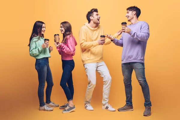 Happy laughing friends talking and holding coffee to go, on yellow — Stock Photo