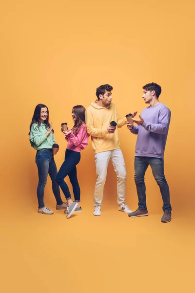 Friends talking and holding disposable cups on coffee break, on yellow — Stock Photo