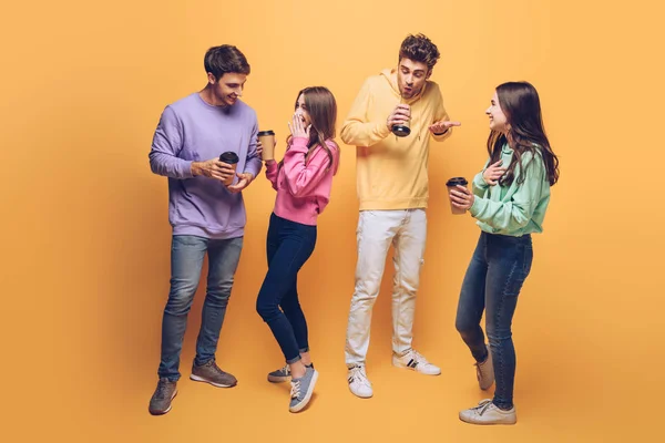 Amigos sorridentes conversando e segurando café para ir juntos, em amarelo — Fotografia de Stock