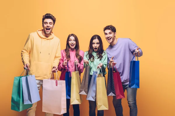 Excited friends holding shopping bags together, isolated on yellow — Stock Photo