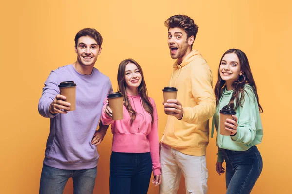 Aufgeregte Freunde zeigen Coffee to go, isoliert auf gelb — Stockfoto