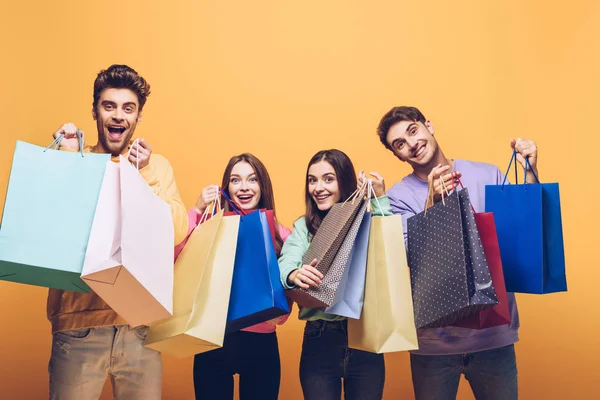 Glückliche Freunde, die Einkaufstüten zusammenhalten, isoliert auf gelb — Stockfoto