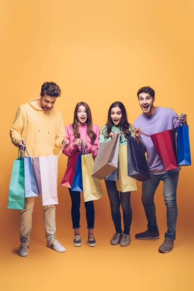 Surpreso jovens amigos segurando sacos de compras juntos, em amarelo — Fotografia de Stock