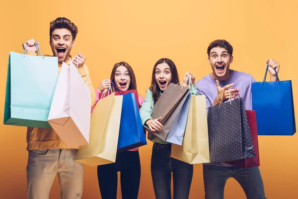 Excited young friends shouting and holding shopping bags together, isolated on yellow — Stock Photo