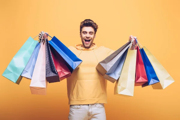 Guapo excitado hombre sosteniendo bolsa de compras, aislado en amarillo - foto de stock