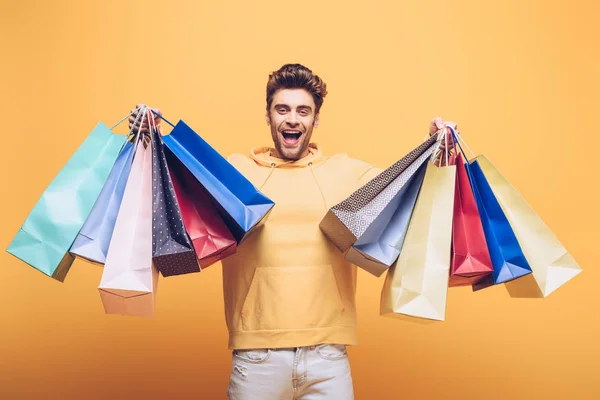 Bel homme excité tenant sac à provisions, isolé sur jaune — Photo de stock