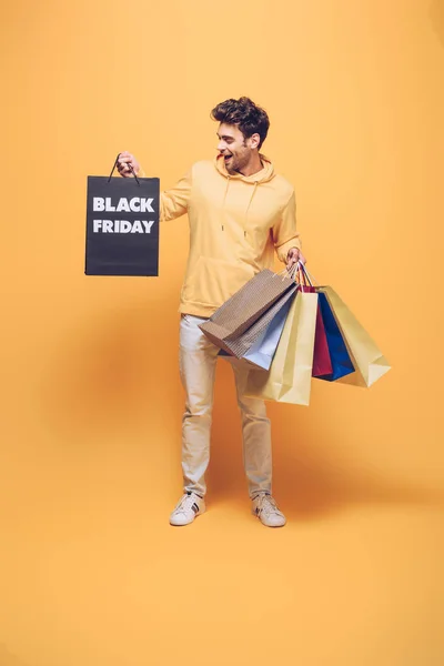 Збуджений чоловік тримає сумки на чорній п'ятниці, на жовтому — стокове фото