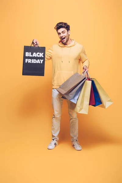 Emotional man holding shopping bags on black friday, on yellow — Stock Photo