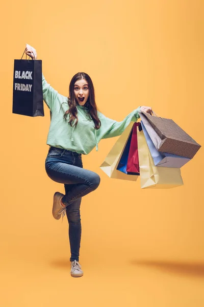 Excited woman jumping and holding shopping bags on black friday, on yellow — Stock Photo