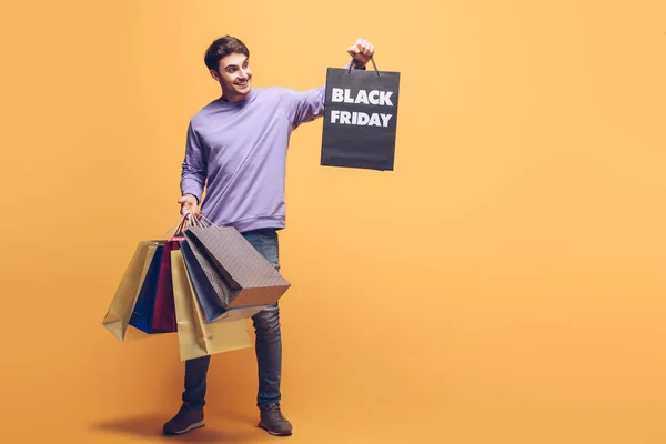 Happy man holding shopping bags on black friday, on yellow — Stock Photo