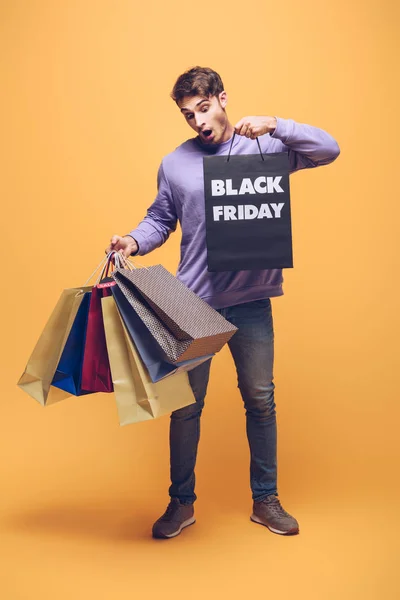 Shocked man holding shopping bags on black friday, on yellow — Stock Photo