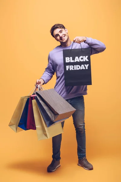 Sonriente hombre sosteniendo bolsas de compras el viernes negro, en amarillo - foto de stock