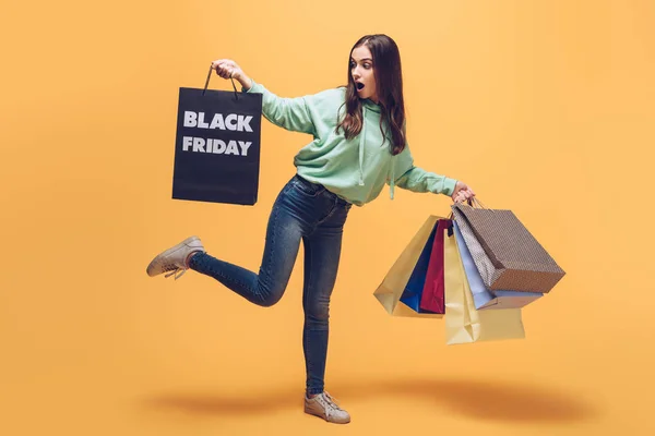 Chocado chica sosteniendo bolsas de compras en negro viernes, en amarillo - foto de stock