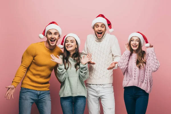 Aufgeregte Freunde in Pullovern und Weihnachtsmützen, vereinzelt auf rosa — Stockfoto