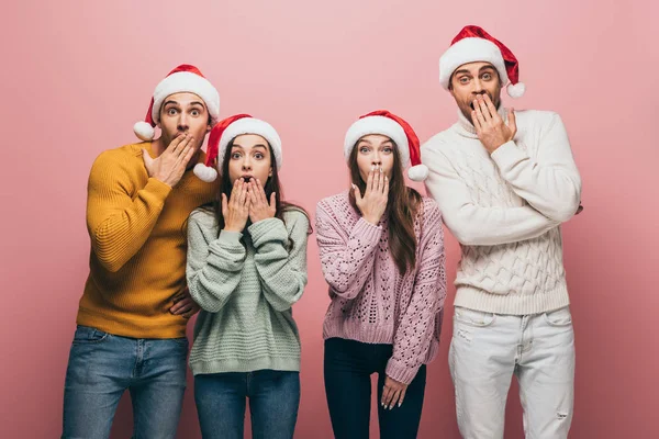 Amigos chocados em suéteres e chapéus de Papai Noel, isolado em rosa — Fotografia de Stock