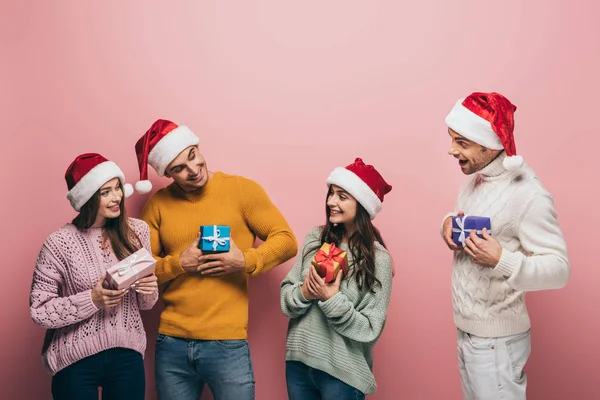 Heureux amis dans santa chapeaux tenant cadeaux de Noël, isolé sur rose — Photo de stock
