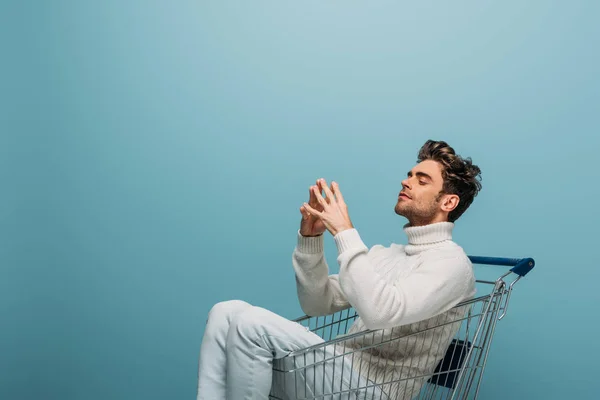 Thoughtful man sitting in shopping cart, isolated on blue — Stock Photo