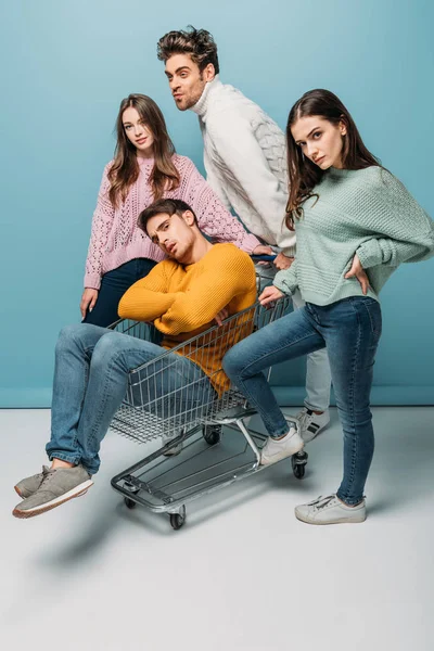 Young funny friends having fun and riding in shopping cart on blue — Stock Photo