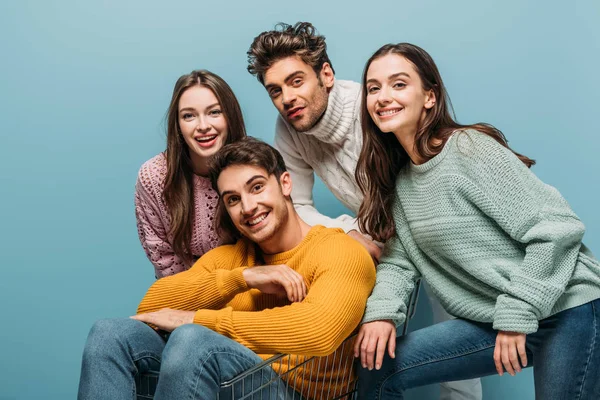 Amigos alegres que se divierten con el carrito de la compra, aislado en azul - foto de stock