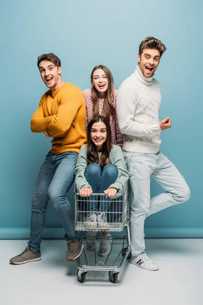 Jóvenes amigos se divierten con el carrito de la compra, en azul - foto de stock