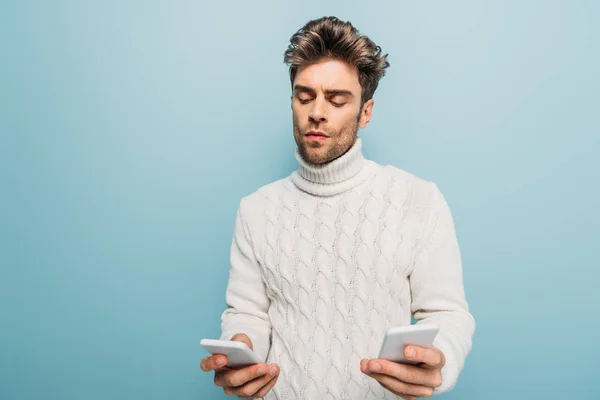 Uomo premuroso utilizzando due smartphone, isolato su blu — Foto stock