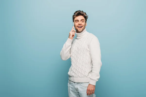 Fröhlicher gutaussehender Mann, der auf dem Smartphone spricht, isoliert auf blauem Grund — Stockfoto