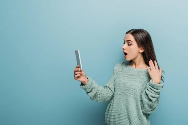 Bela mulher chocada usando smartphone, isolado no azul — Fotografia de Stock