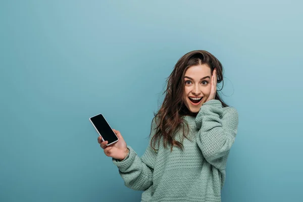 Збуджена жінка тримає смартфон з порожнім екраном, ізольована на синьому — стокове фото