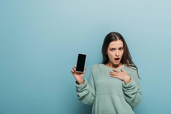 Schockierte Frau zeigt Smartphone mit leerem Bildschirm, isoliert auf blauem Grund — Stockfoto