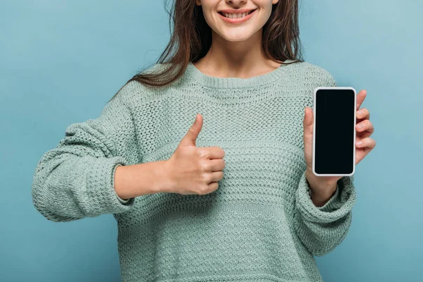 Vue recadrée de la femme souriante montrant pouce levé et smartphone avec écran blanc, isolé sur bleu — Photo de stock