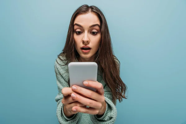 Chica sorprendida usando teléfono inteligente, aislado en azul - foto de stock