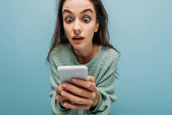 Потрясенная женщина смотрит на смартфон, изолированный на синий — стоковое фото