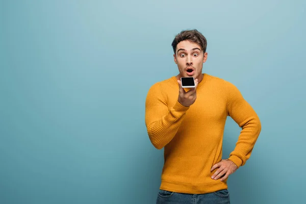 Shocked handsome man using smartphone, isolated on blue — Stock Photo