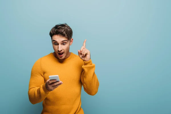 Homem surpreso usando smartphone e tendo ideia, isolado em azul — Fotografia de Stock