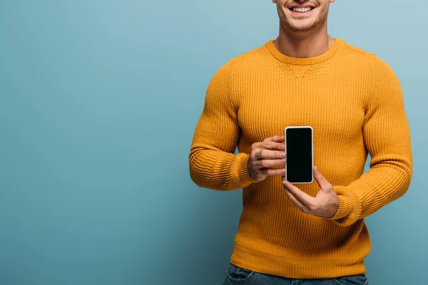 Vista recortada del hombre sonriente que muestra el teléfono inteligente con pantalla en blanco, aislado en azul - foto de stock