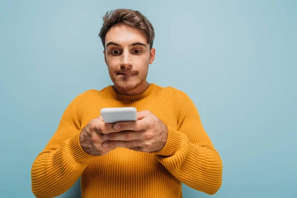 Schöner fokussierter Mann mit Smartphone, isoliert auf blauem Grund — Stockfoto