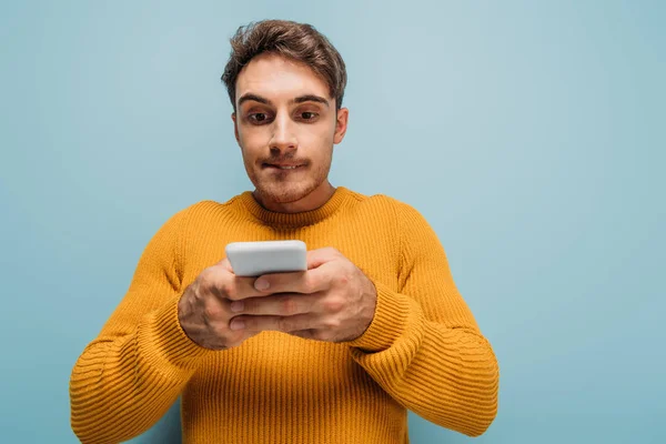 Hombre enfocado guapo usando teléfono inteligente, aislado en azul - foto de stock