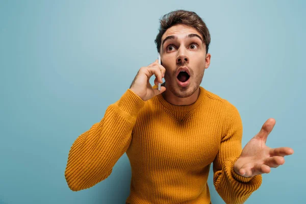 Überraschter gutaussehender Mann spricht auf Smartphone, isoliert auf blauem Grund — Stockfoto